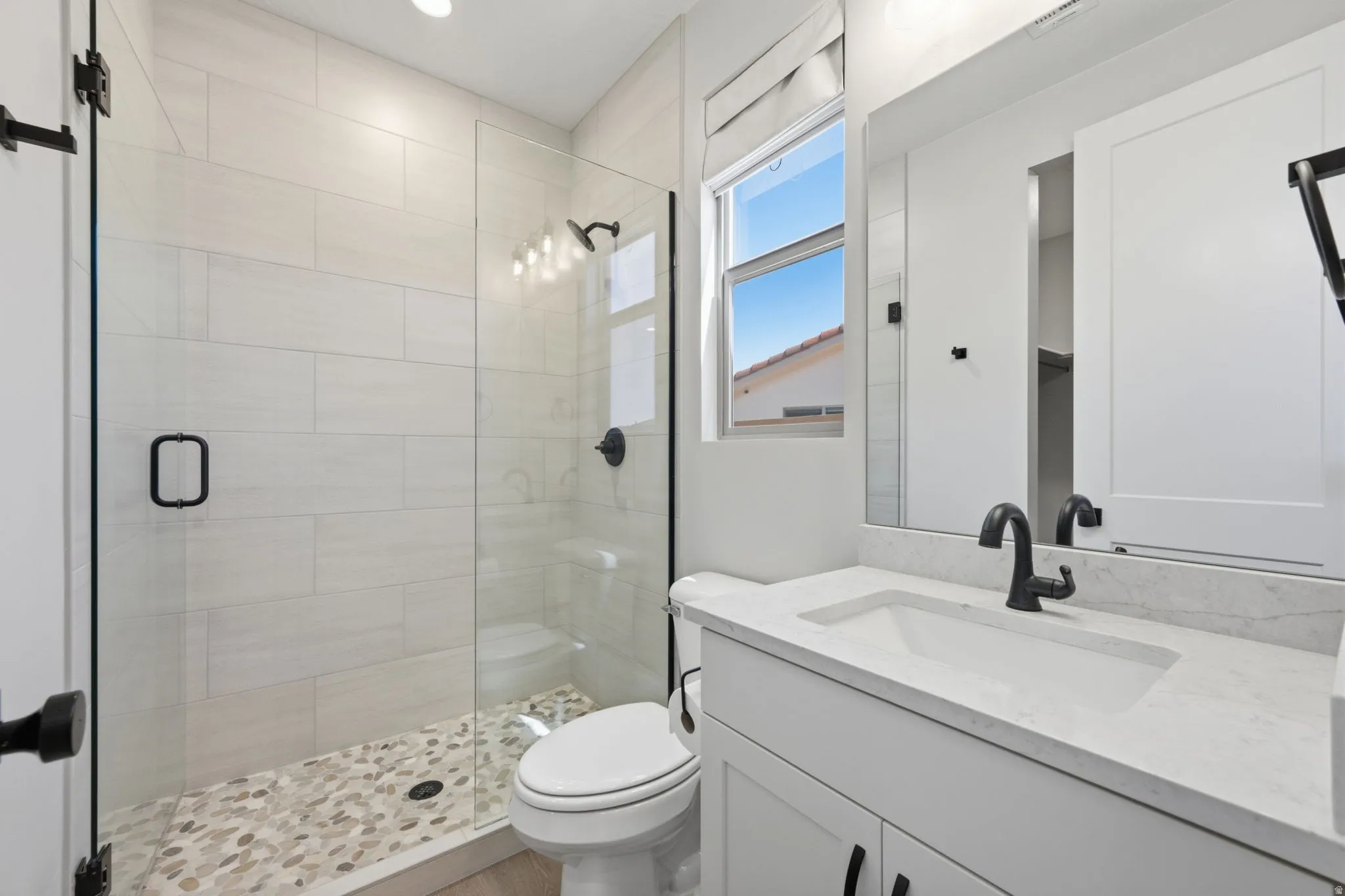 Glass-enclosed shower with pebble-finish flooring and subway tile surround, alongside a vanity with an integrated sink and quartz countertop