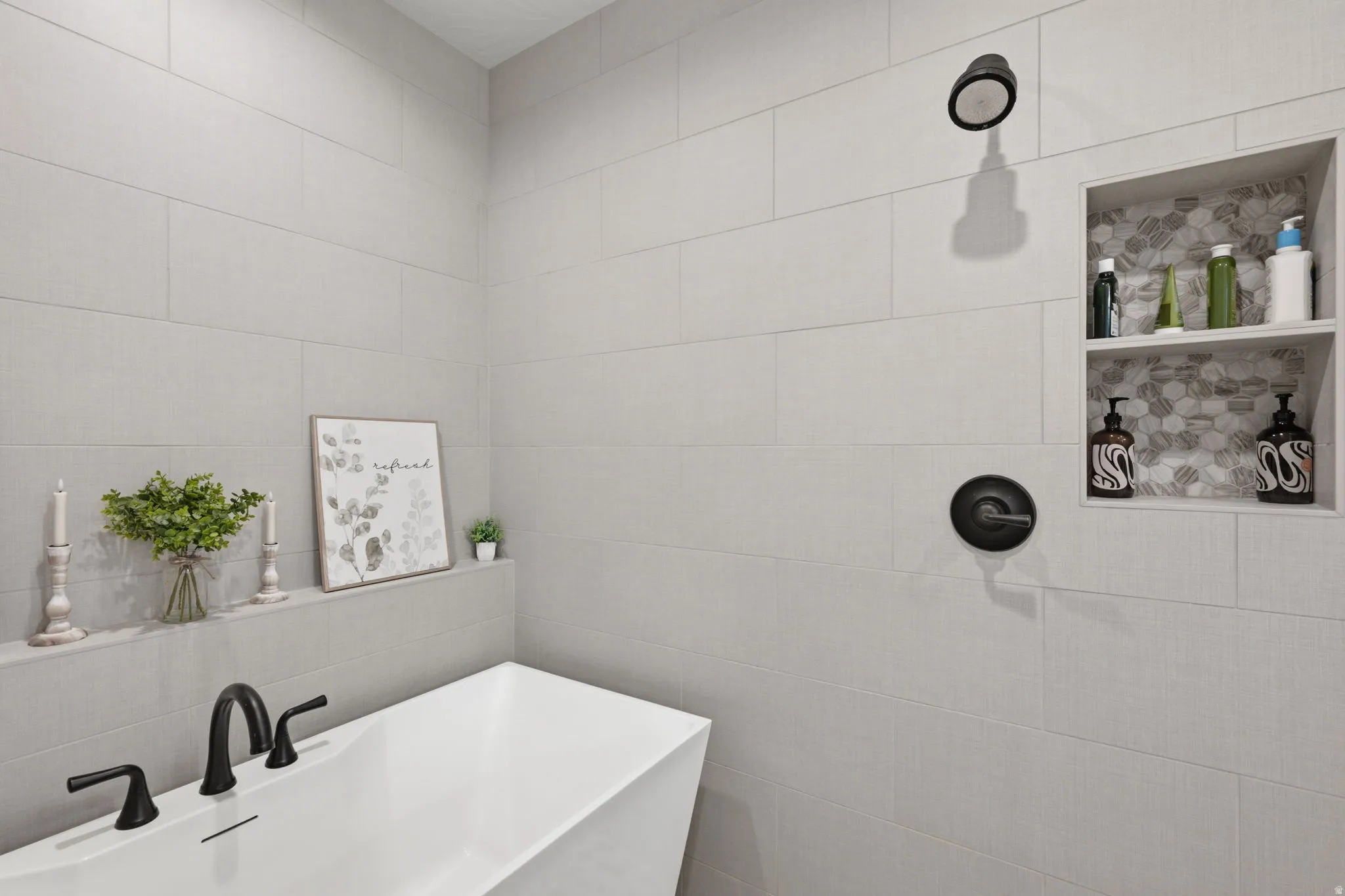 Freestanding soaking tub with matte black fixtures, full-height tile shower surround, and a recessed shower niche with mosaic tile
