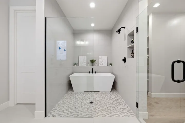 Walk-in shower with a glass enclosure, free standing tub, white hexagon tile flooring, and matte black fixtures
