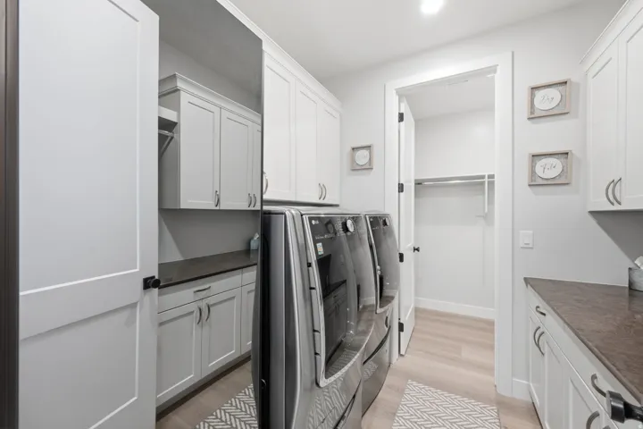 Laundry room featuring extensive white cabinetry, dark countertops, wood-finish flooring, and a built-in hanging rod