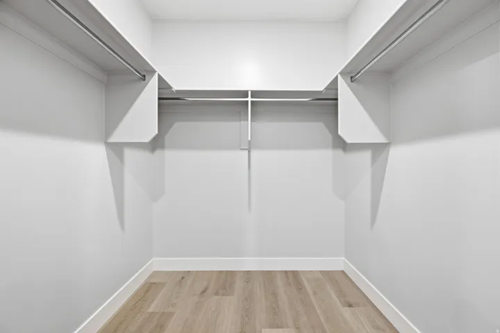 Walk-in closet featuring LVP wood-finish flooring, white walls, and built-in shelving with hanging rods