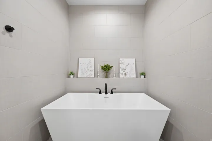 Freestanding soaking tub with matte black fixtures, integrated shelving, and full-height tiled walls