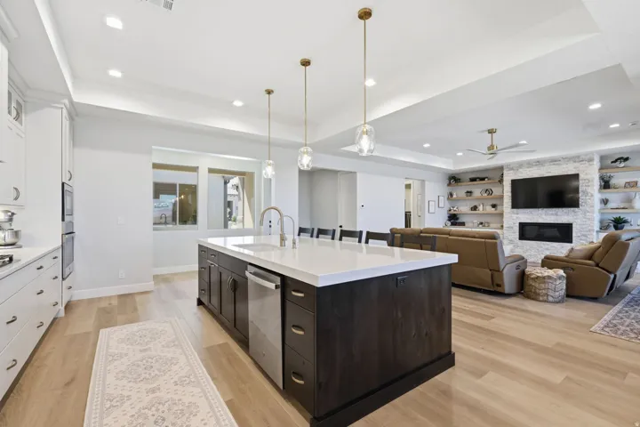 Open-concept kitchen and living area featuring LVP wood-finish flooring, a large kitchen island with a white countertop, and a living space with a fireplace and built-in shelving