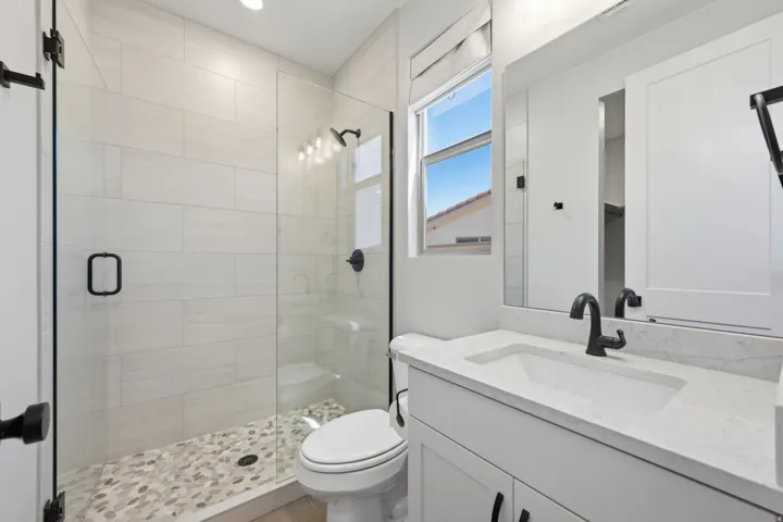 Glass-enclosed shower with pebble-finish flooring and subway tile surround, alongside a vanity with an integrated sink and quartz countertop