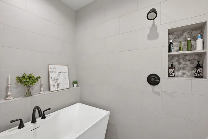 Freestanding soaking tub with matte black fixtures, full-height tile shower surround, and a recessed shower niche with mosaic tile