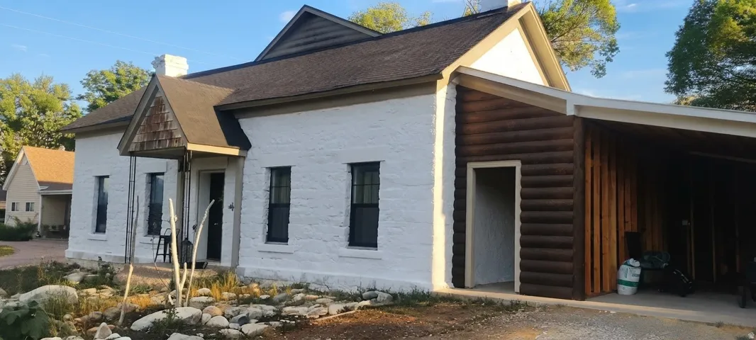 White stone exterior with black-framed windows, a covered entry with wood shingle siding, and an attached log-sided carport