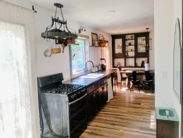 Kitchen featuring wood-finish flooring, dark wood cabinetry, a stainless steel range, a pot rack light fixture, and a built-in display cabinet
