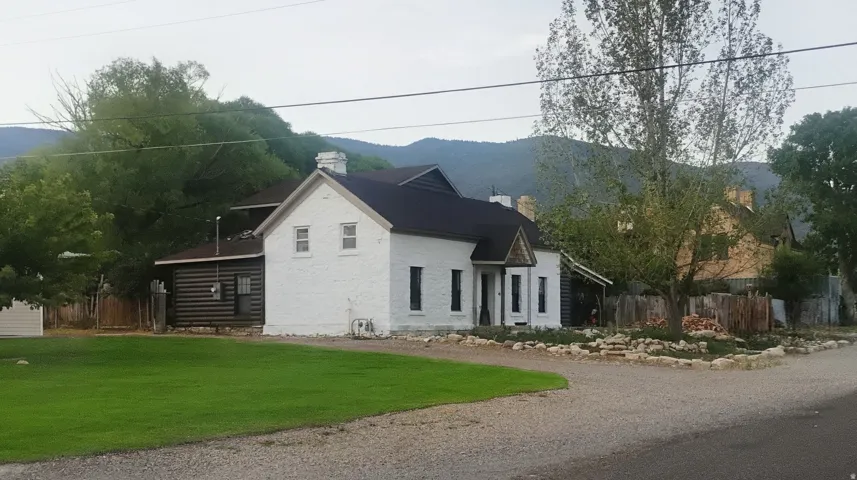 White exterior with dark trim and log siding accents, dark roof, front gravel area, and a green lawn