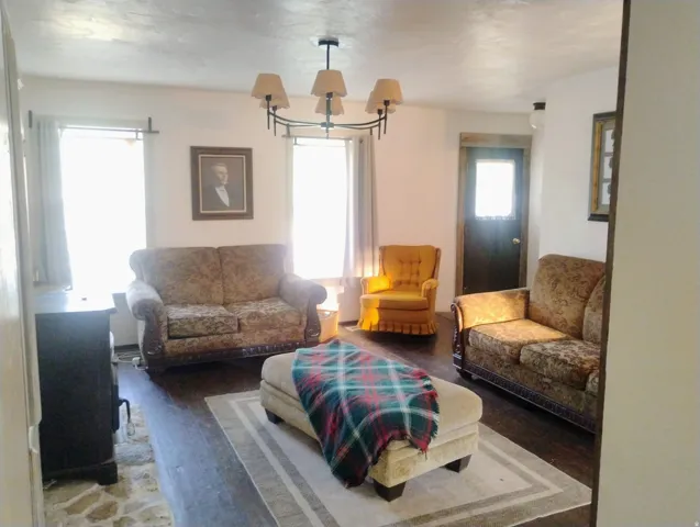 Living area featuring wood-finish flooring, a contemporary chandelier, and a dark-toned entry door with a frosted glass panel