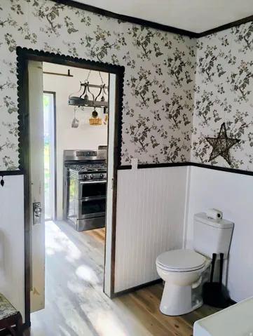 Wallpapered walls with contrasting dark trim, paneled wainscoting, and wood-finish flooring