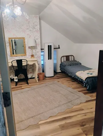 Sloped ceiling design, wood-finish flooring, accent wall with patterned wallpaper, built-in wall-mounted lighting fixture, and a compact window