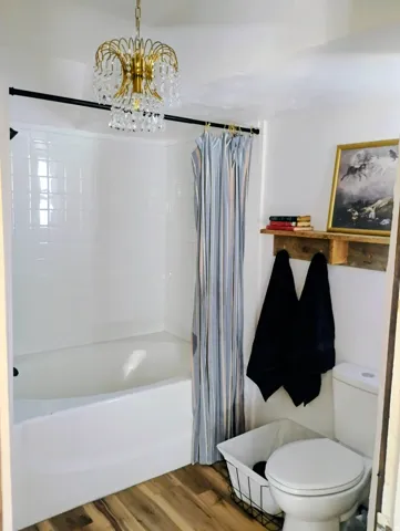 Bathtub with white subway tile surround, wood-finish flooring, and a crystal chandelier