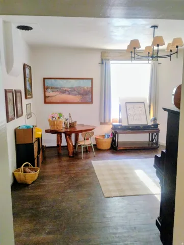 Wood-finish flooring throughout, with a window featuring light-colored drapes, and a multi-arm chandelier with shade covers
