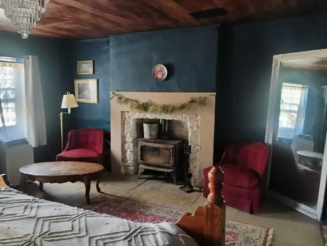 Stone fireplace with a built-in wood-burning stove, dark wood-finish ceiling, and a multi-tiered chandelier