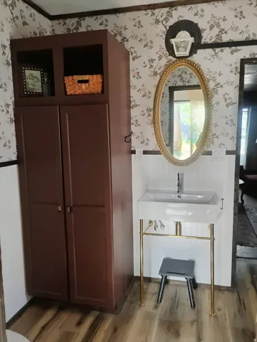 Pedestal sink with brass-finish legs, wood-finish flooring, and wall-mounted vanity light
