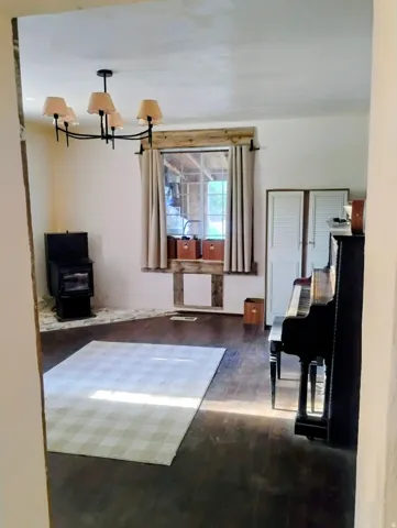 Wood-finish flooring, central window with wood trim, black chandelier with multiple light sources, and louvered double doors