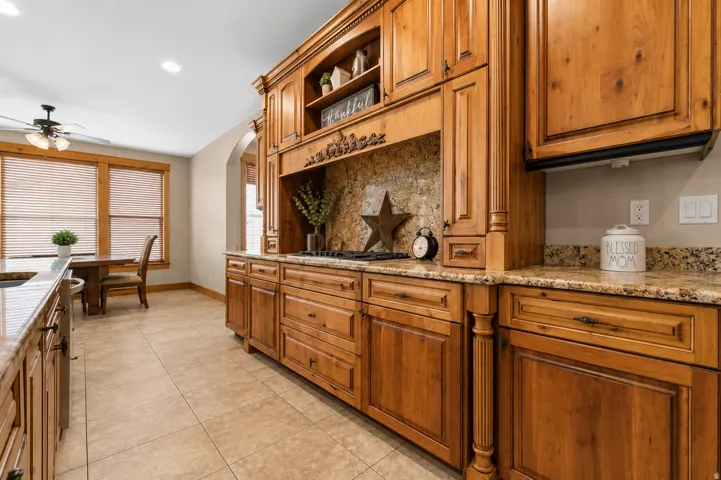 Custom wood cabinetry, stone countertops, integrated cooktop, tiled flooring, and an arched doorway