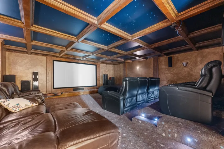 Movie theater - Coffered ceiling featuring a starry sky motif, wall-mounted projector screen, built-in wall sconces, and multi-level flooring with recessed lighting