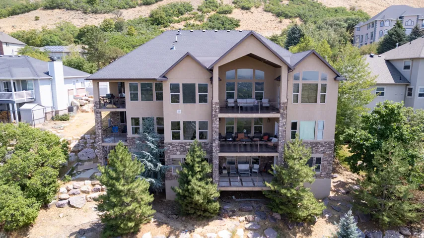 Back view - Multi-level stucco and stone exterior featuring multiple balconies with metal railings, a ground-level patio, and a gabled roofline