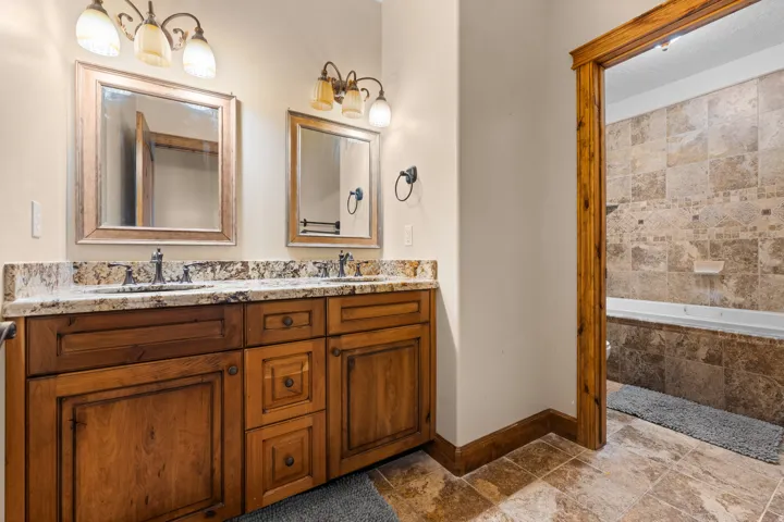 Dual wood-finish vanities with stone countertops, individual framed mirrors, and overhead light fixtures