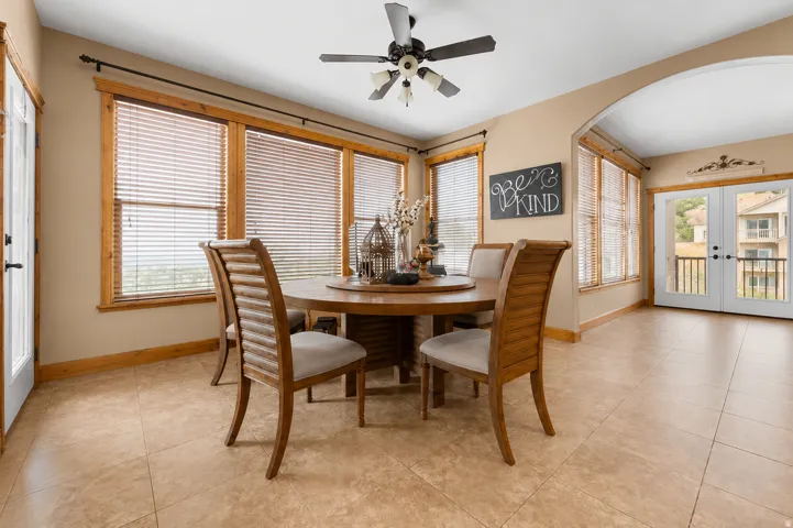Eat in kitchen - Tiled flooring, multiple large windows with wood trim, archway, ceiling fan with integrated lighting, and white French doors