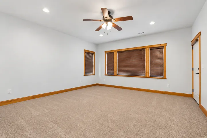 Spacious room with plush carpeting, three windows with wood trim, a ceiling fan, and recessed lighting