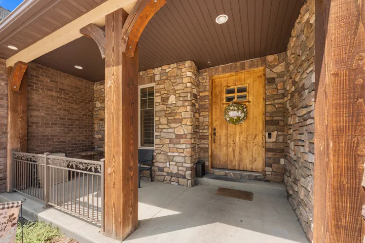 Main entrance - Stone facade with a paneled wood-finish door, covered porch, and exposed wood beams