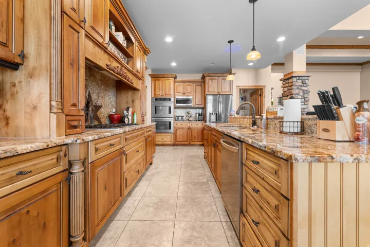 Kitchen featuring natural wood cabinetry, light-toned granite countertops, tile flooring, and stainless steel appliances
