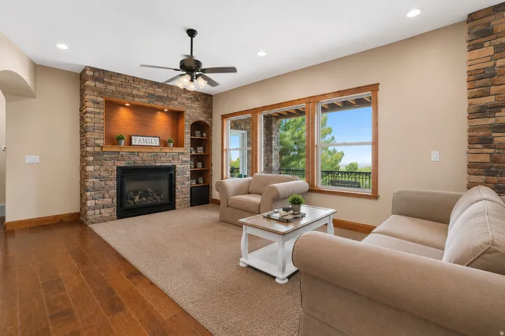 Stone-clad fireplace with a wood mantle and built-in shelving, wood-finish flooring, recessed lighting, and a ceiling fan