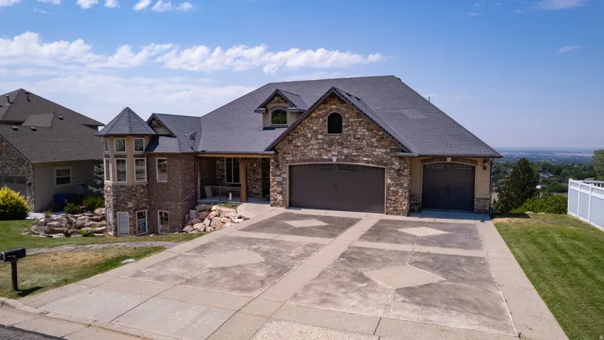 Stone and brick facade with a prominent turret, multi-car garage, stamped concrete driveway, and a fenced side yard