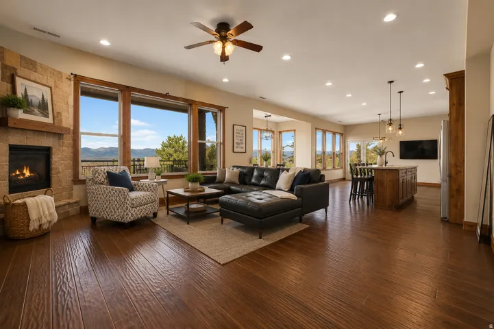 Open-concept living area featuring wood-finish flooring, a stone-clad fireplace with a wood mantle, recessed lighting, and large windows (AI staged-structure and integrity not changed)