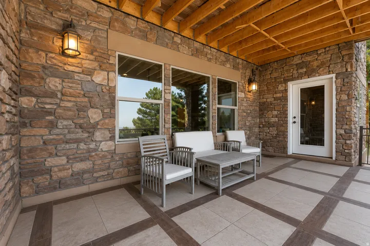 Covered patio featuring a stone veneer wall, exposed wood beam ceiling, decorative wall sconces, and a glass-paneled exterior door