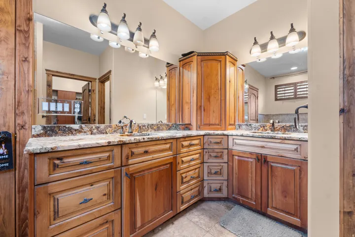 Dual vanity with granite countertops, wood-finish cabinetry, and built-in corner storage