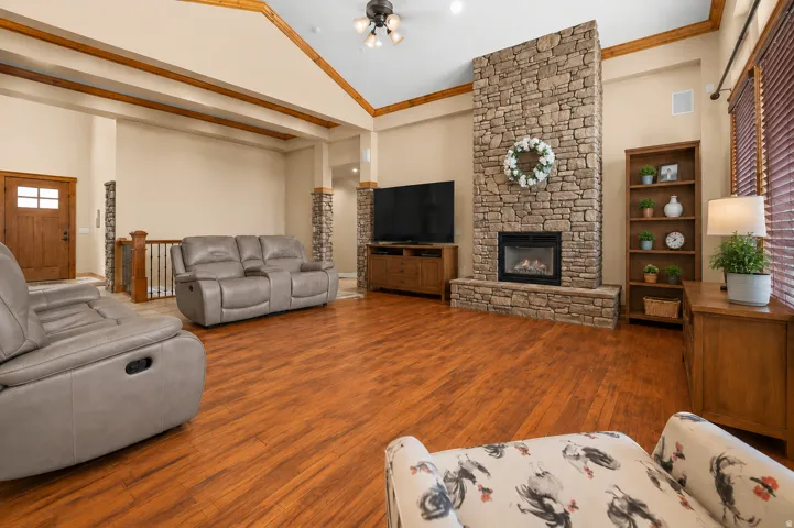 Varnished wood-finish flooring, vaulted ceiling with exposed wood beams, stone-clad fireplace, a solid wood entry door with glass inserts