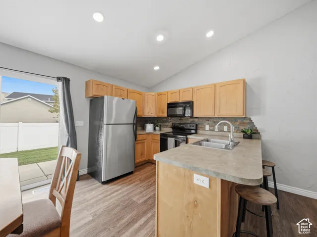 Kitchen featuring stainless steel appliances, wood-finish cabinetry, a stone-finish backsplash, and a breakfast bar