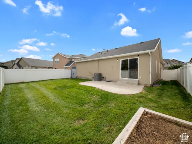 Expansive backyard featuring a manicured lawn, a concrete patio, a sliding glass door, a built-in planter box, and a white vinyl privacy fence