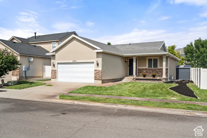 Single-story exterior featuring stucco and stone veneer accents, an attached garage, a covered front entry, a concrete driveway, and a fenced side yard