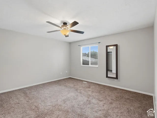 Neutral tone wall paint, textured carpet flooring, window with horizontal blinds, and a ceiling fan with integrated lighting