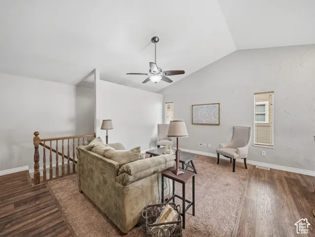 Vaulted ceiling with ceiling fan, wood-finish flooring, and a natural wood staircase railing