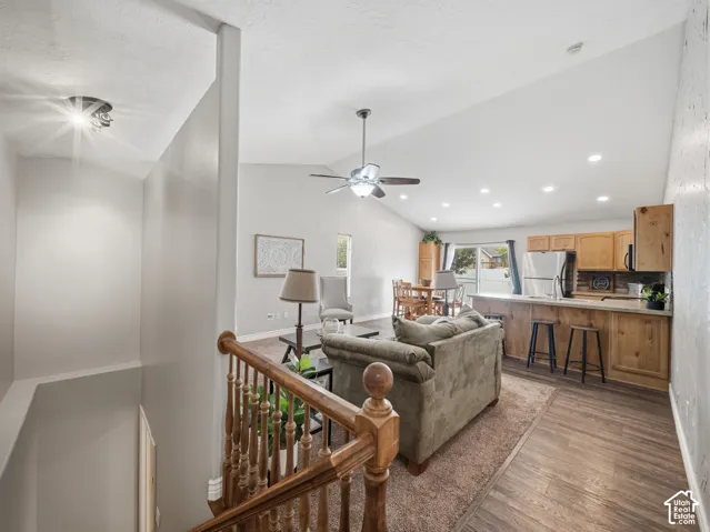 Vaulted ceiling with recessed lighting and a ceiling fan, wood-finish flooring, staircase with wood banister, and a kitchen island with wood paneling