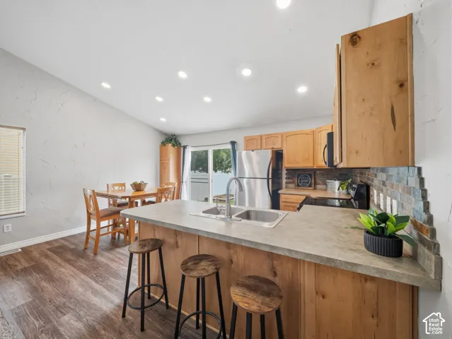 Vaulted ceiling with recessed lighting, wood-finish flooring, wood cabinetry, stainless steel appliances, and a tiled backsplash