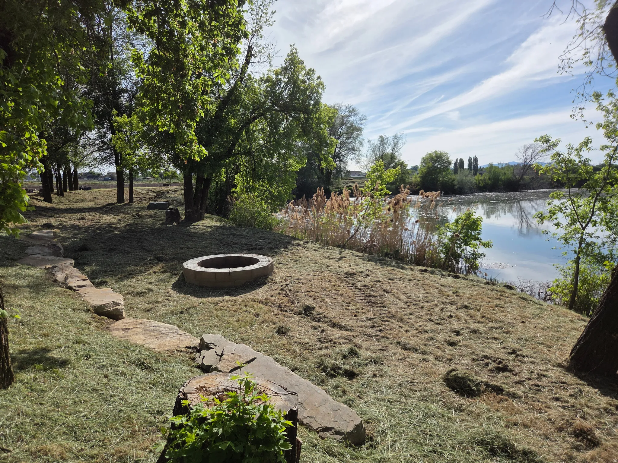 Waterfront property featuring a stone fire pit, stone pathway, and mature trees