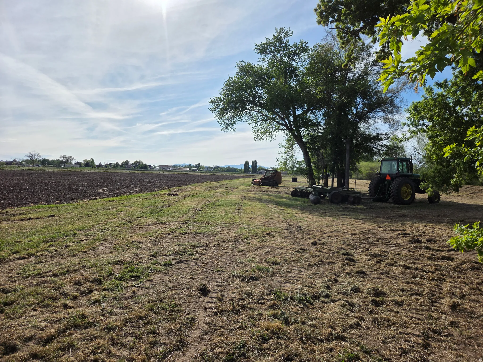 Expansive open field with cultivated land, mature trees, and a clear sky backdrop