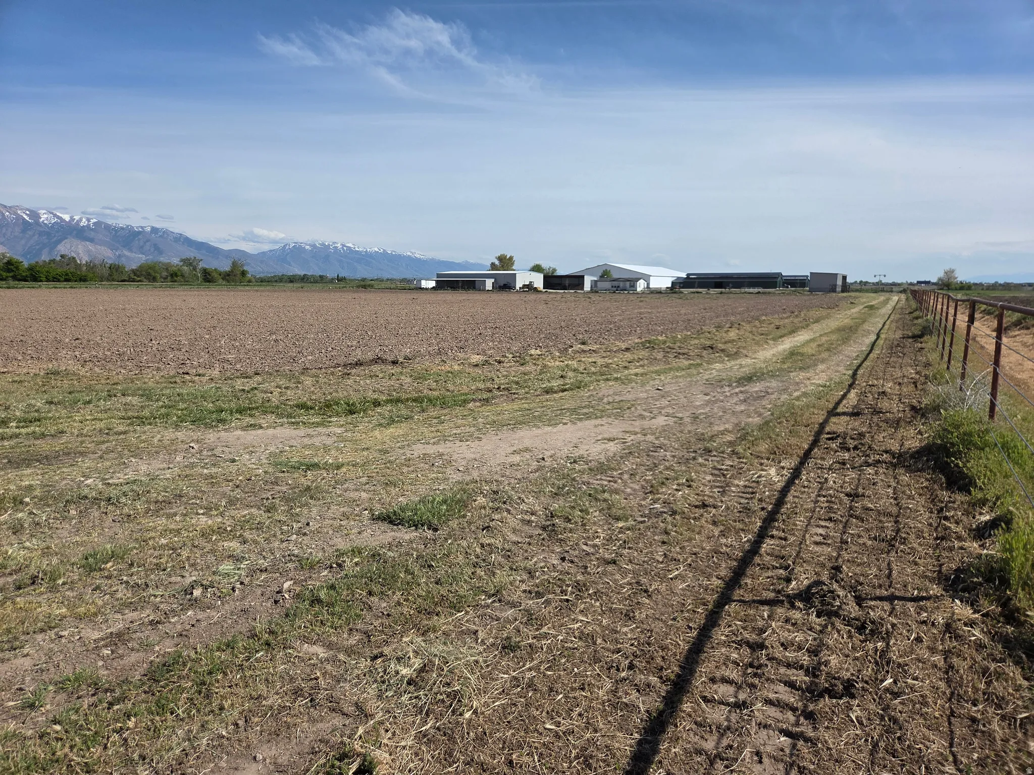Expansive tilled field with distant mountains and a perimeter fence