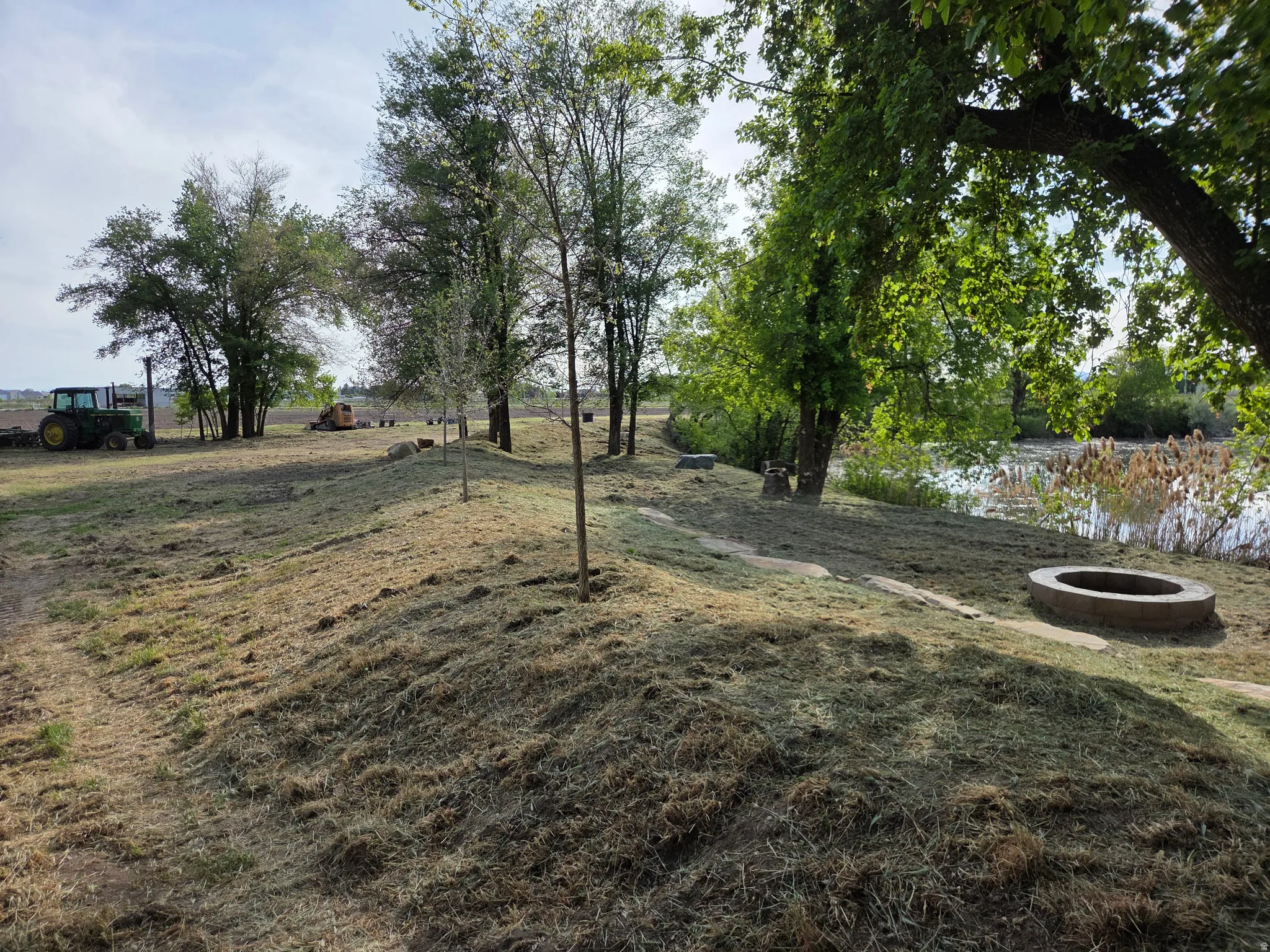 Expansive outdoor space featuring a body of water, mature trees, and a fire pit