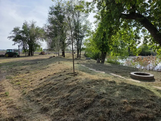 Expansive outdoor space featuring a body of water, mature trees, and a fire pit