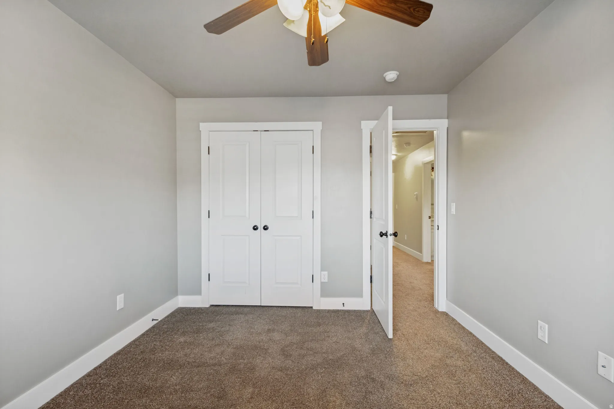 Carpeted flooring, white trim, dual closet doors with black hardware, and a ceiling fan with integrated lighting