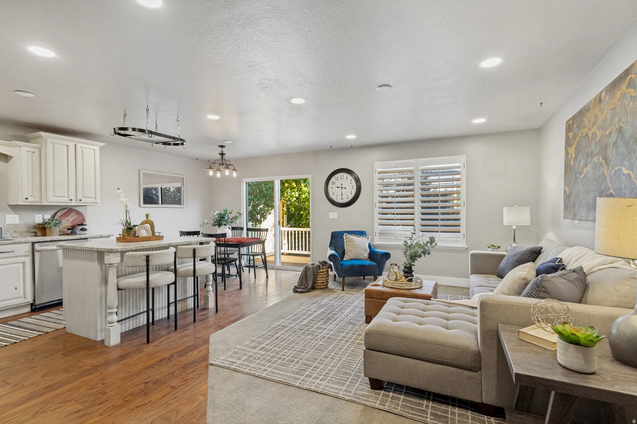 Open-concept living area featuring wood-finish flooring, a kitchen island with seating, white cabinetry, and sliding glass door onto a large deck