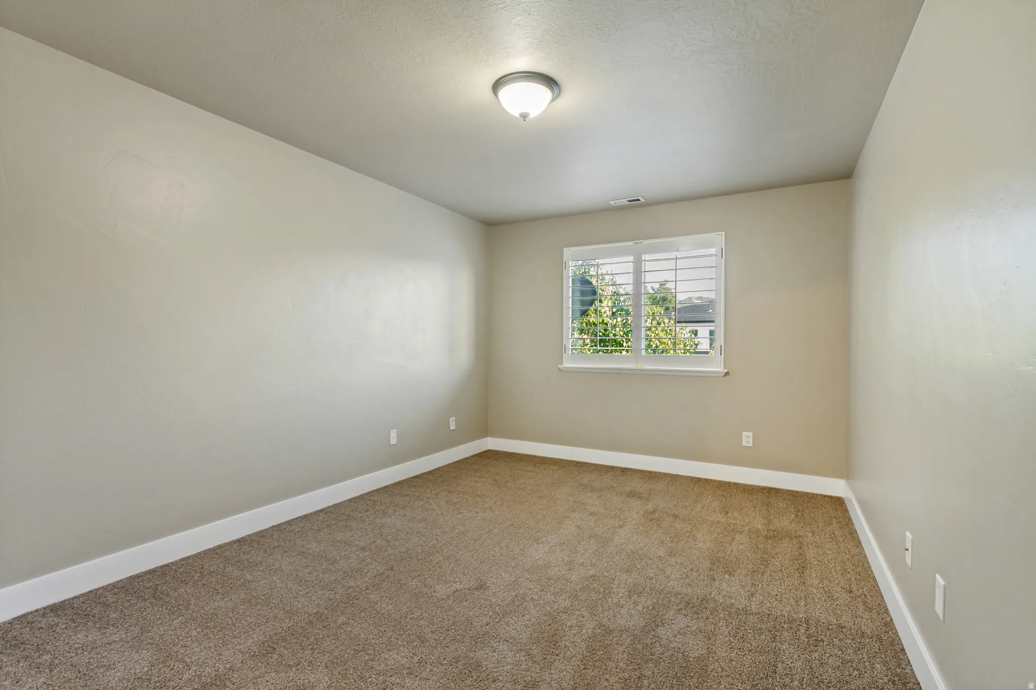 Wall-to-wall carpeting, light neutral wall color, white trim, window with white blinds, and a flush-mount ceiling light fixture