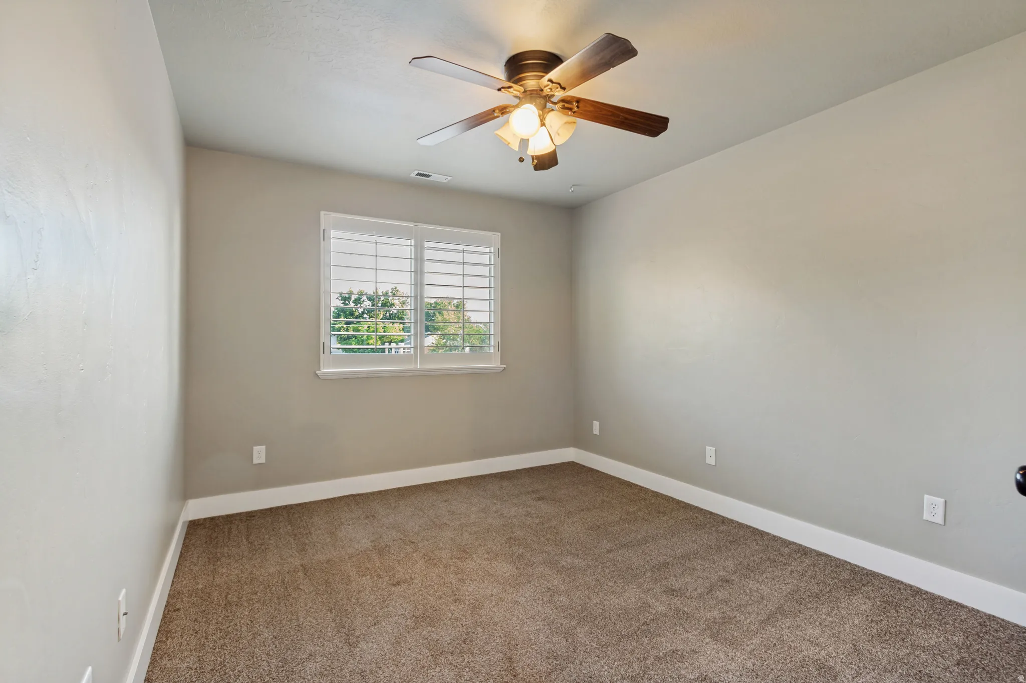 Carpeted room featuring a window with plantation shutters, a ceiling fan with integrated lighting, and neutral wall tones